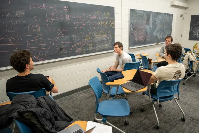 students seated near front of classroom discussing problem on chalkboard