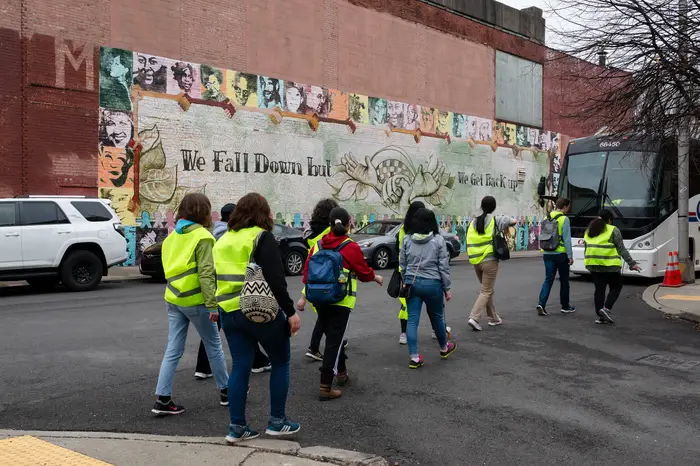 students walking to bus in front of large mural on side of building