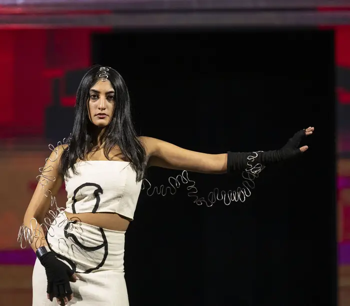 Model wears white skirt and crop top with twisted metal wire accents along her body, arms and head.