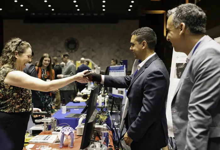 A Congressional staffer shakes the hand of a researcher wearing a special glove that controls a robot