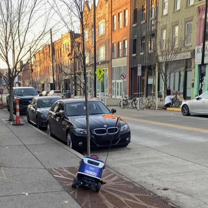 A personal delivery device stuck in a grate requires human assistance to regain mobility.