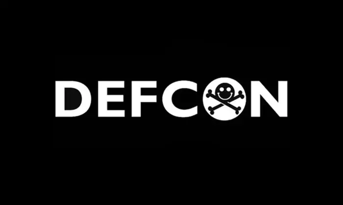 Black field with white letters spelling out "DEFCON" with the center of the "o" including a smiley face and crossbones to form the DEF CON logo. 