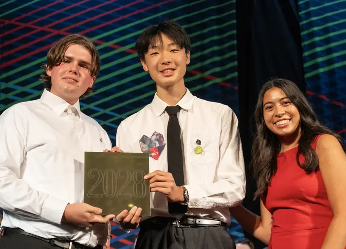 Three people holding a golden tile.