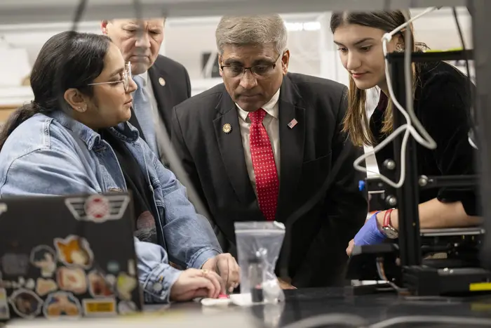 Sethuraman Panchanathan looking closely at experiment with three others