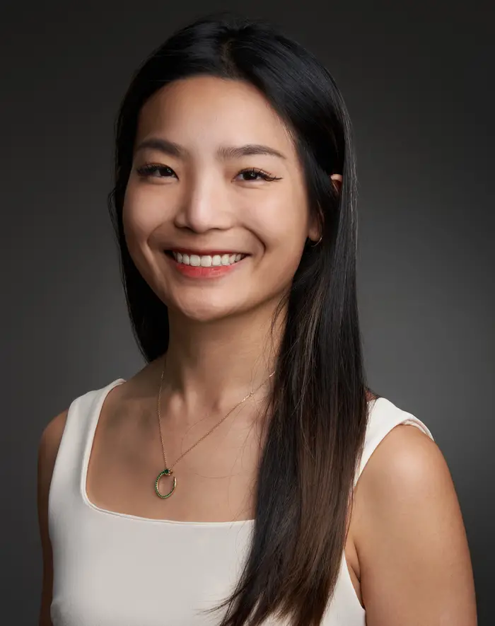 Headshot of a smiling woman with long black hair wearing a white tank top