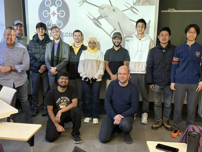 A group photo of people in front of a projector screen showing a drone. 