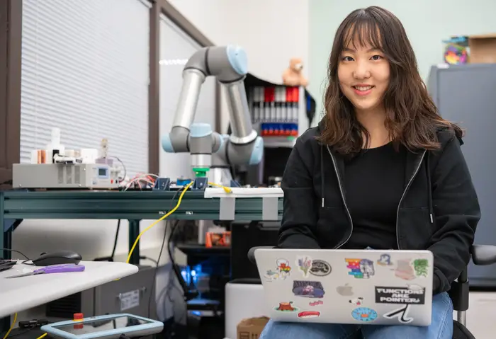 Tiffany Han seated in lab holding laptop