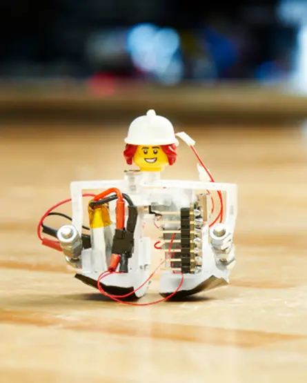 A miniature walking robot with actuators for feet and a lego head and hardhat.