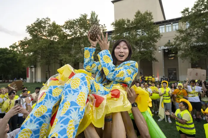 A crowd hoists a woman holding a pineapple.