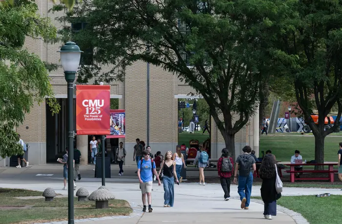 Students walk on CMU campus past a red banner that reads CMU 125 Power of Possibilities.