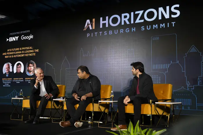 Three people sit in chairs in front of a wall that reads "AI Horizons."