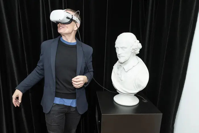 A man wears a VR headset next to a bust of Shakespeare. 
