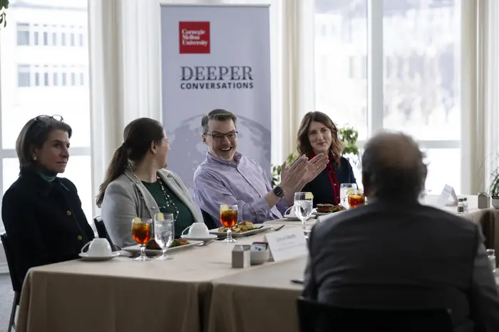 A group of people sitting around tables speaks. 
