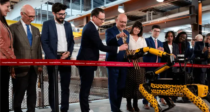 Several people standing near a robotic dog behind a red ribbon during the RIC building opening