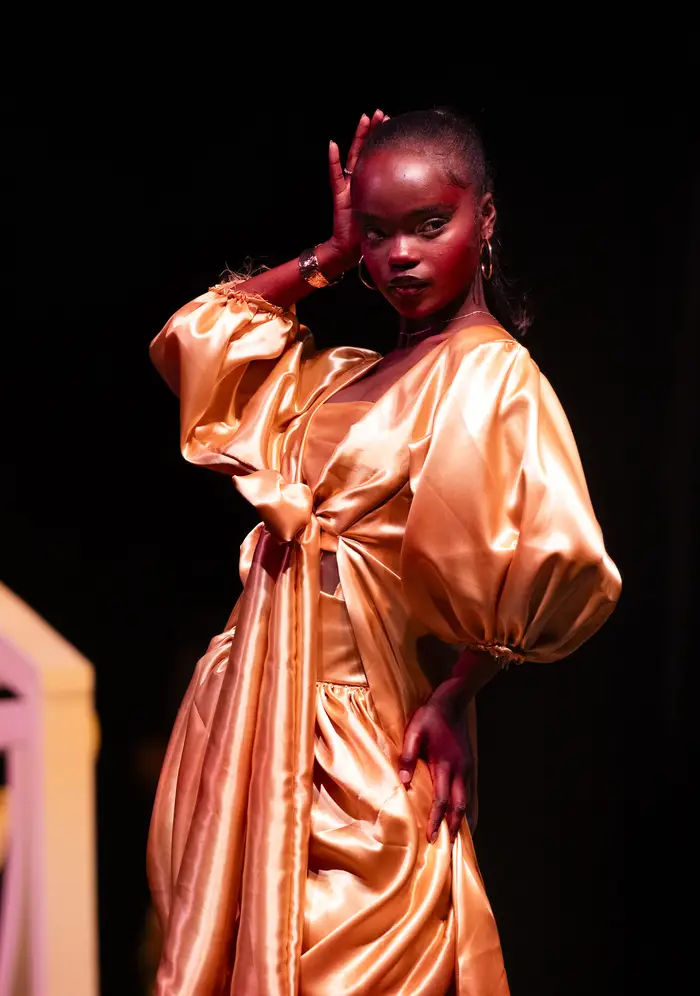 Model wearing a shimmering, draped copper-colored organza gown that tapers at her midsection contrasted with billowing sleeves