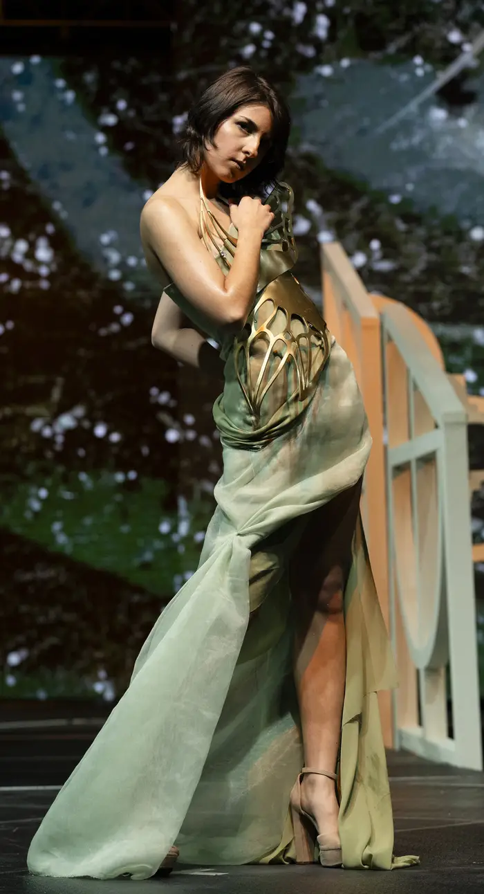 A model is wearing a golden butterfly-wing corset, with a long flowing pale green skirt