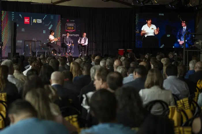 A room full of seated people watching three people converse onstage. 