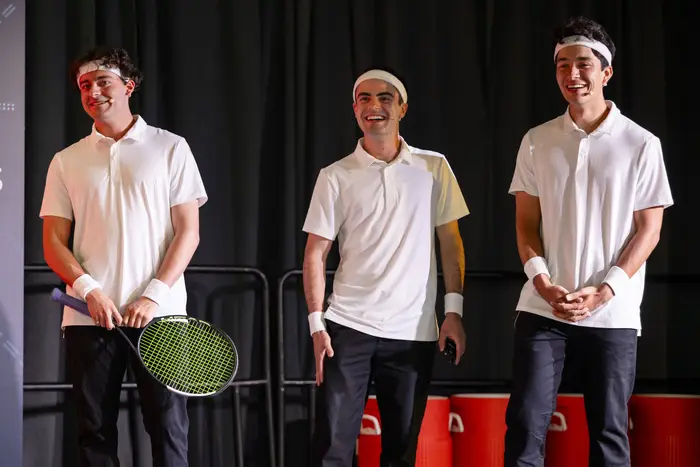 Three men onstage wear tennis garb. 