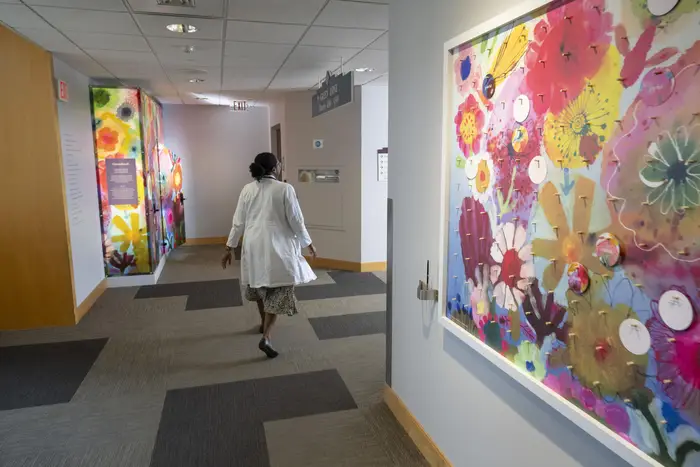 A worker walks through a hallway featuring a multi-colored wall display of art and a multi-colored pod with an open door
