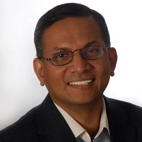 A man with dark hair wearing glasses a dark jacket and white shirt smiles for the camera.