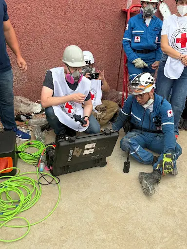 Darwin Mick drives the snake robot from a remote location while rescue workers and civilians look at the images returned from the front of the snake robot.