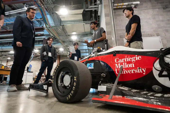 Arya Lohia (second from right) explains Carnegie Mellon Racing’s work on the 26x car during the IROS demos..