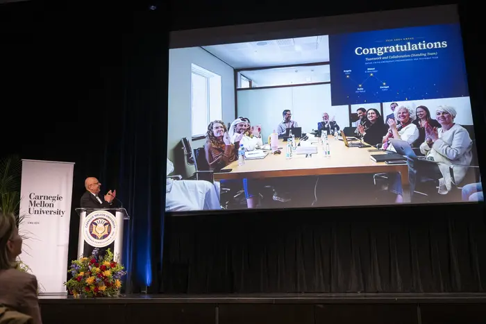 Farnam Jahanian applauds the team in Qatar on screen.