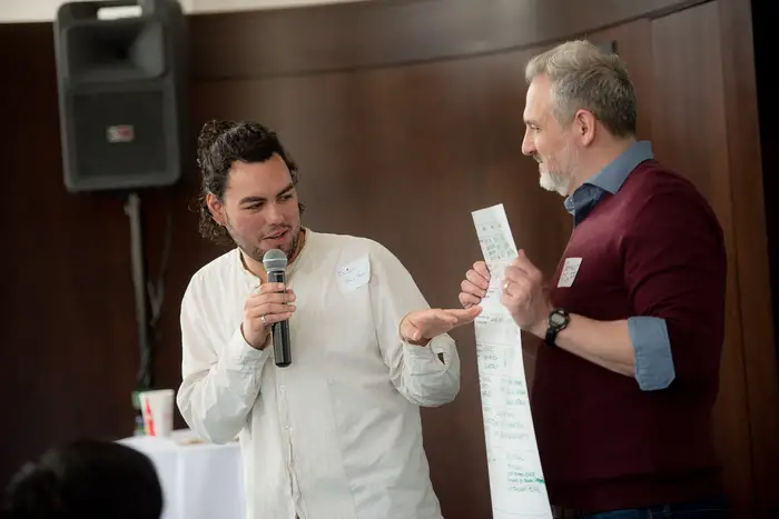 Two men standing in the front of a room with a large piece of paper