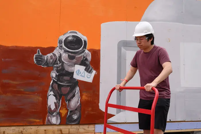 Male student walks past a painting of an astronaut giving a thumbs up