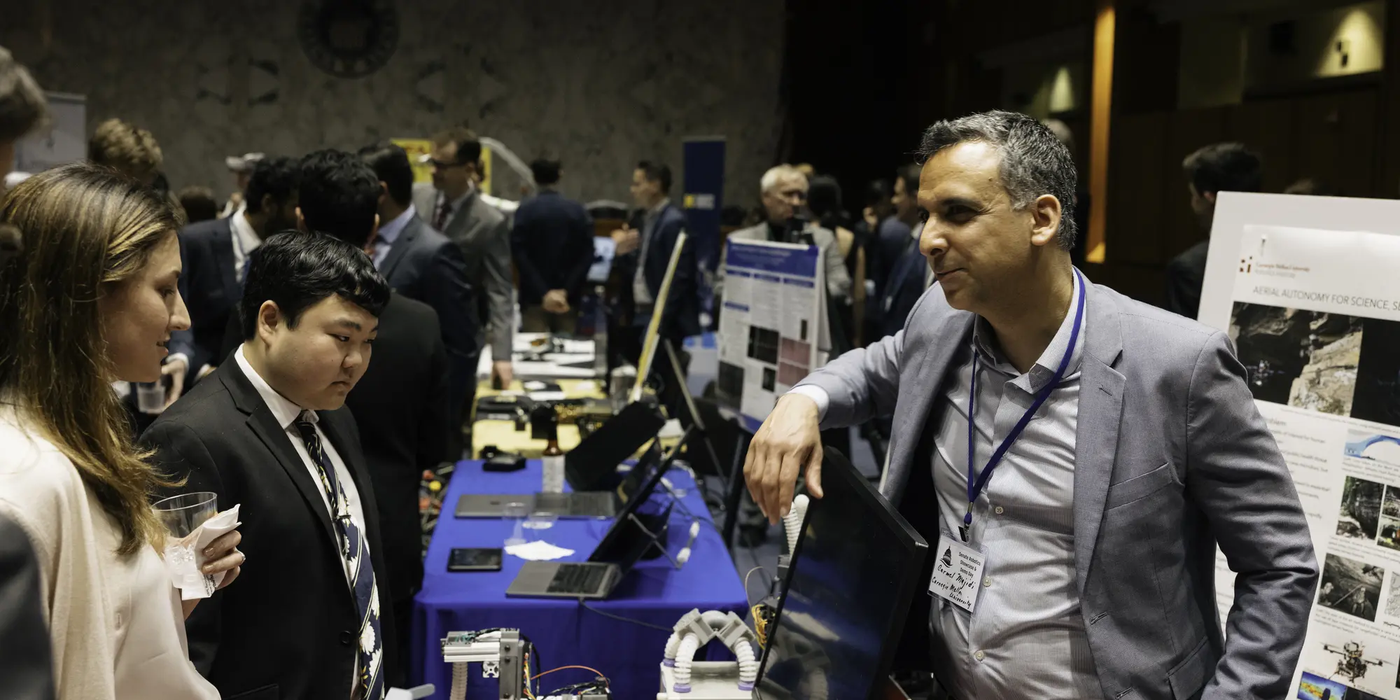 Carmel Majidi (right) talks to people visiting CMU's table at the Robotics Showcase