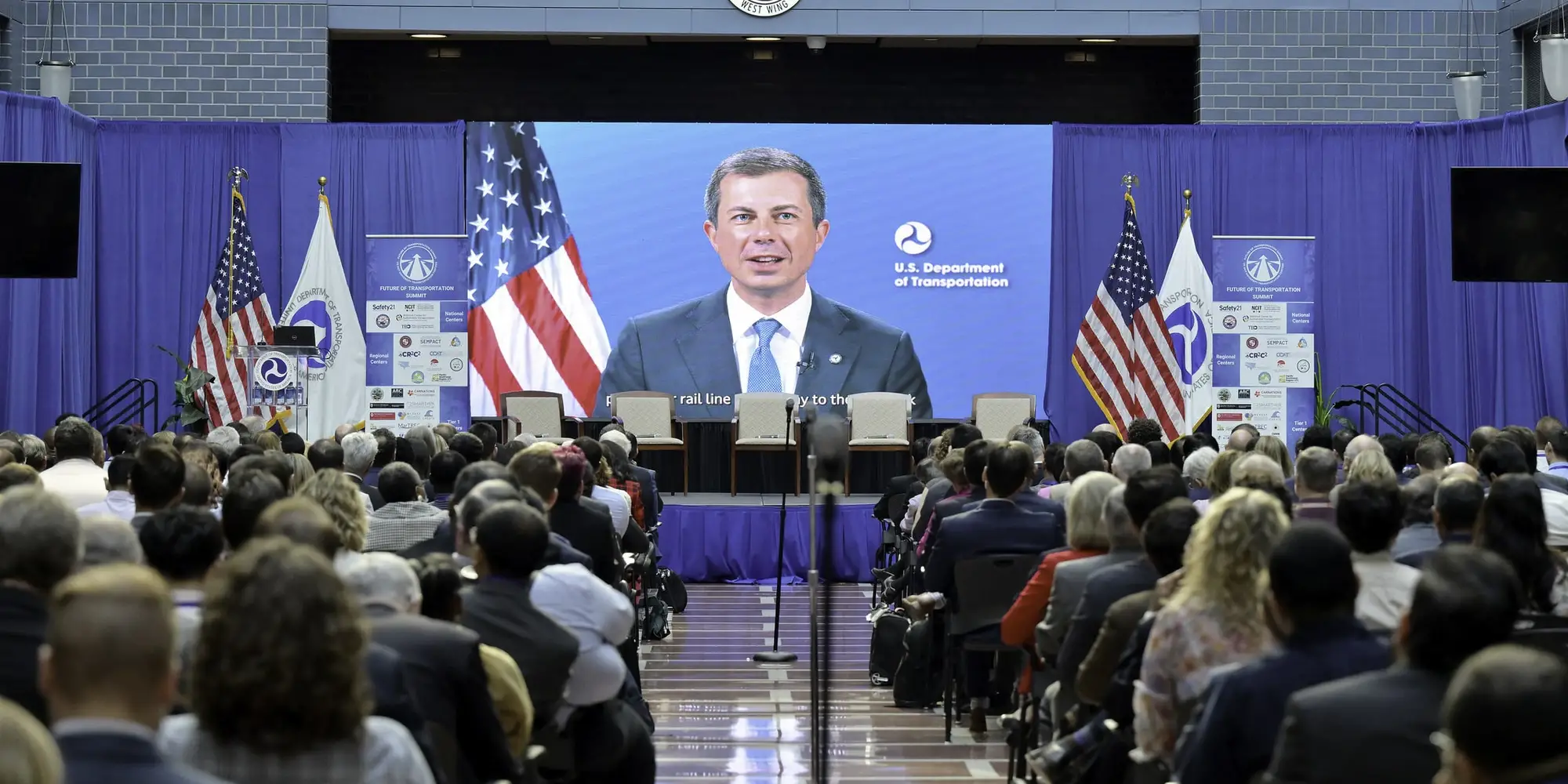 U.S. Secretary of Transportation Pete Buttigieg appears on screen at transportation summit