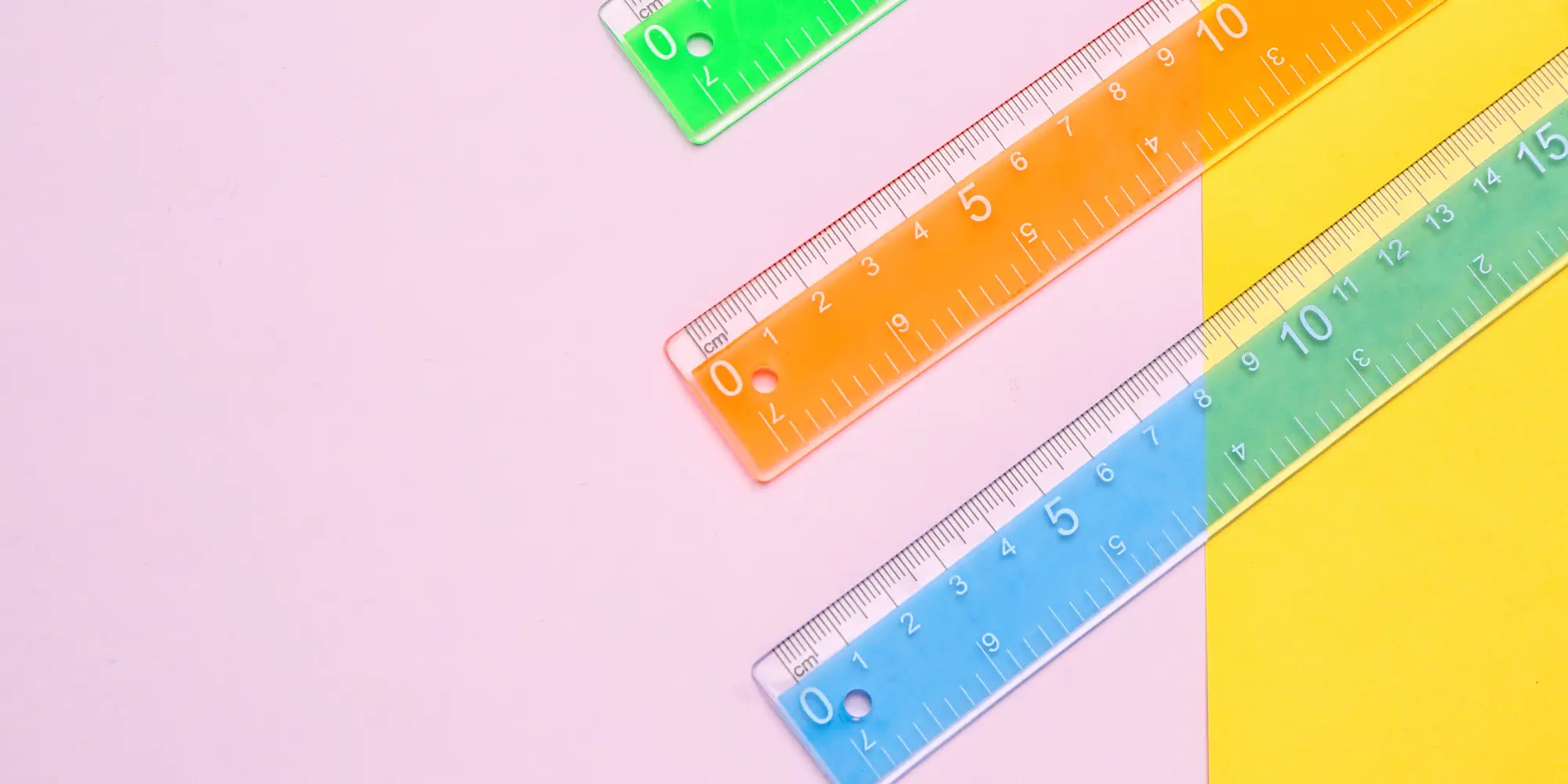 three plastic rules placed diagonally on a pink and yellow background
