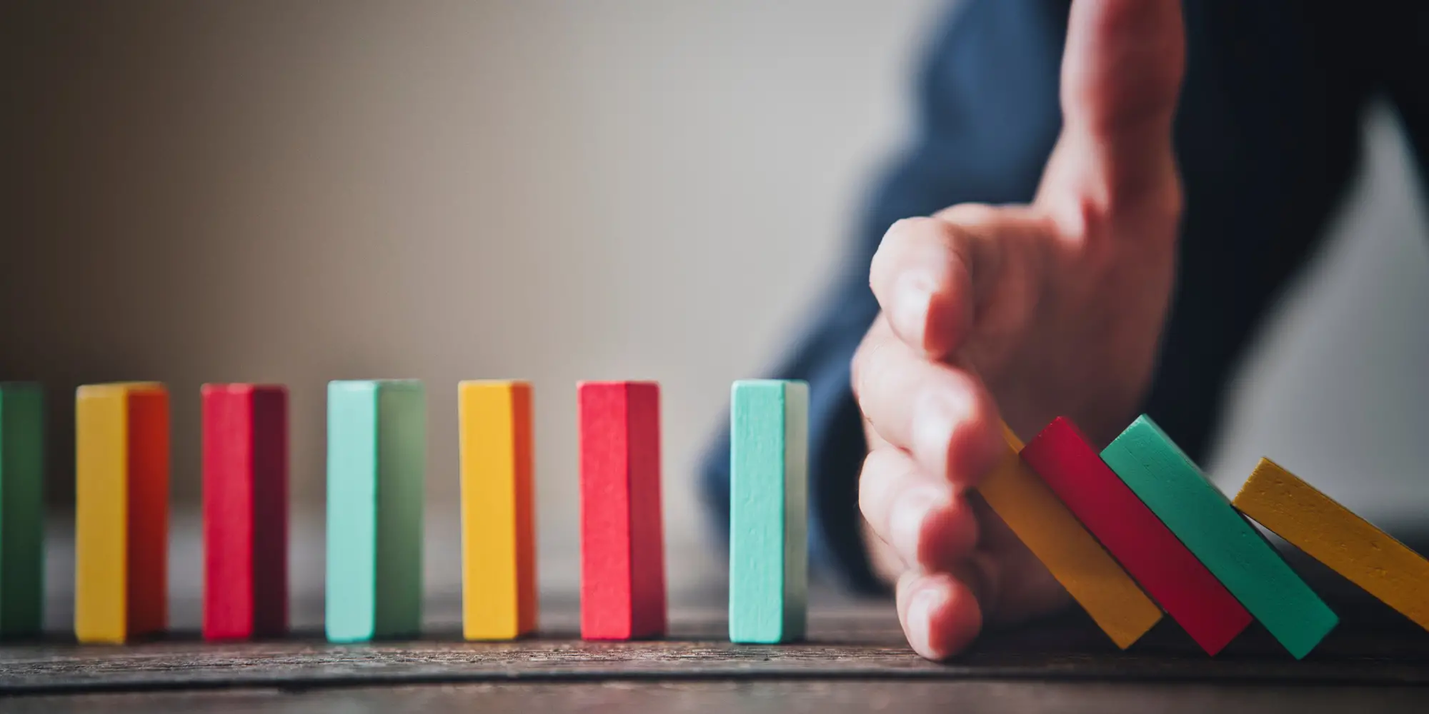 colorful dominos in a line with a hand in the middle to stop some from falling