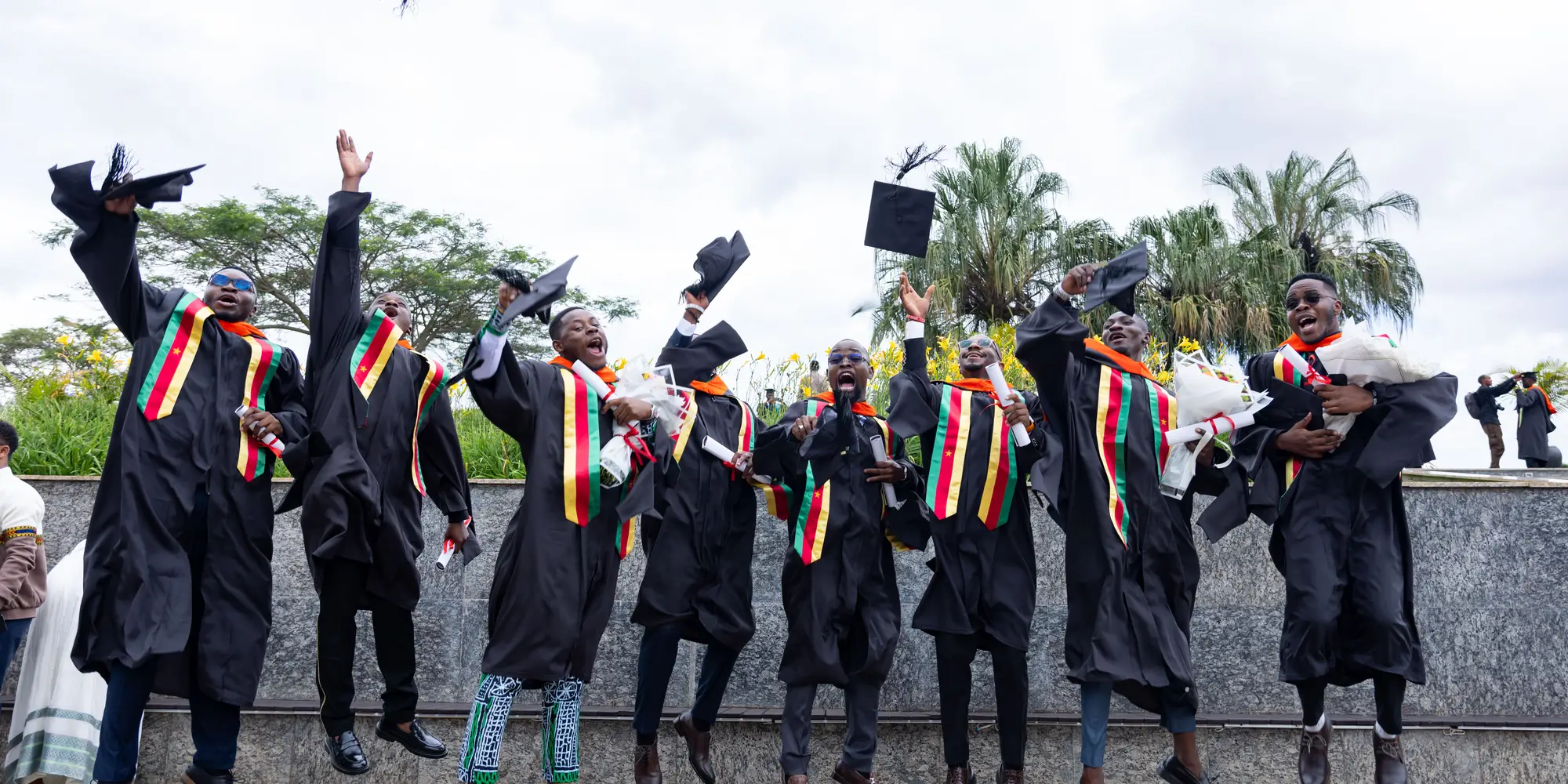 CMU-Africa students in caps and gowns jump and cheer.
