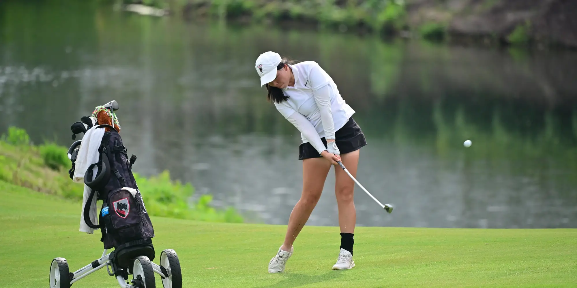 A golfer hits a ball next to a lake.