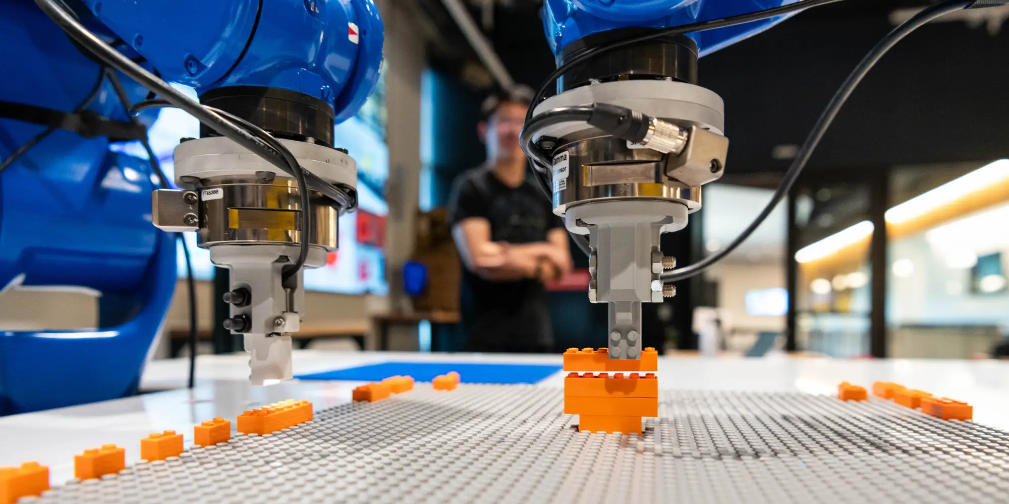 Two blue robotic arms build an orange lego guitar