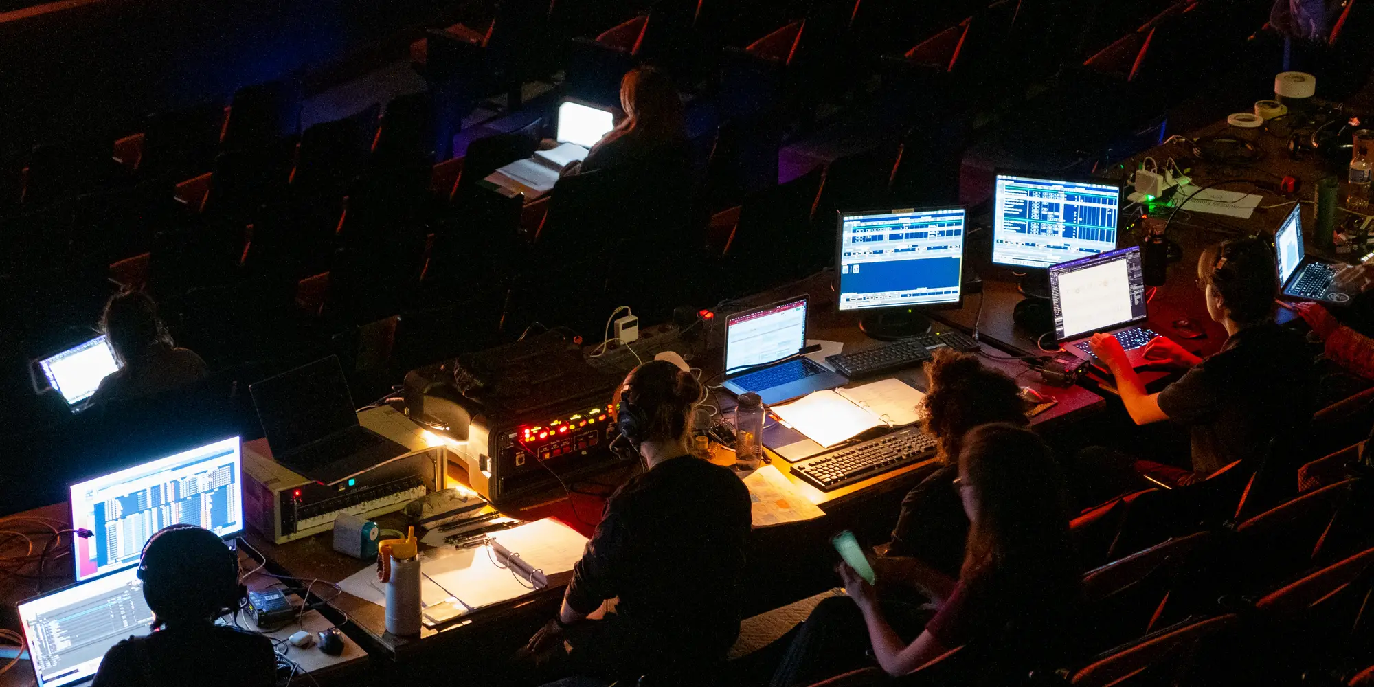 Silhouettes of students sit behind computer screens with their backs to the calendar in a darkened theater.