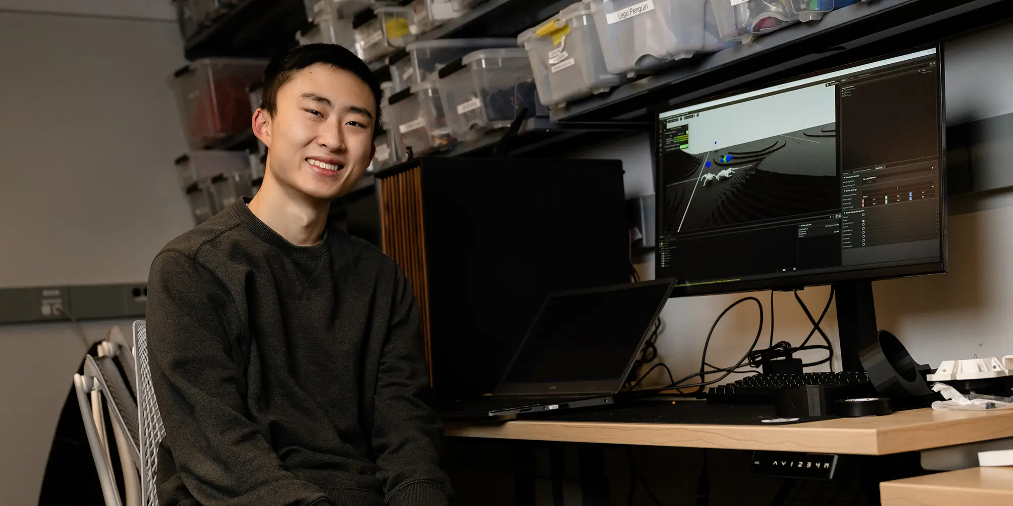 Leo Wang seated next to robotic dog simulation on computer screen