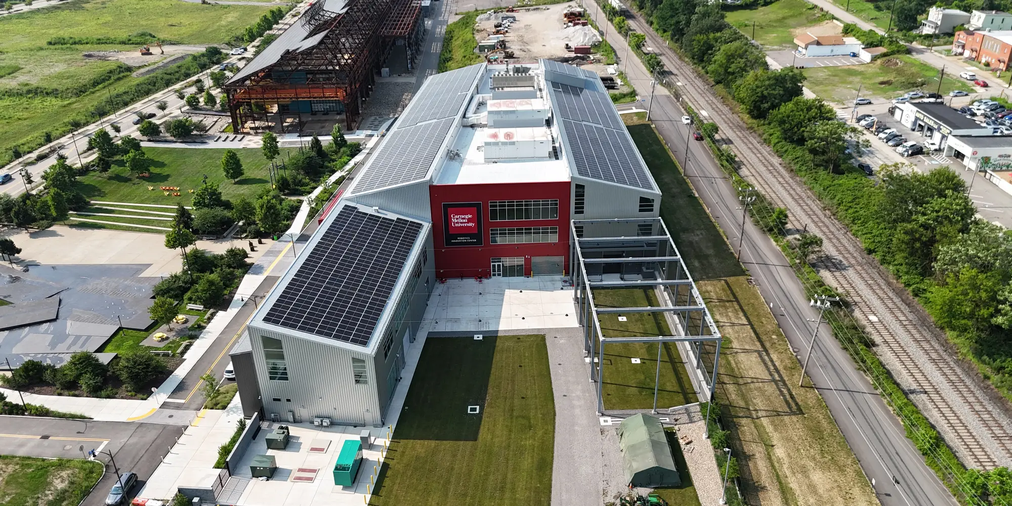 A drone photo from high above the Robotics Innovation Center shows the entire building and the solar array on the roof, as well as the roads and railroad tracks alongside the building and parts of Hazelwood Green and Hazelwood nearby.