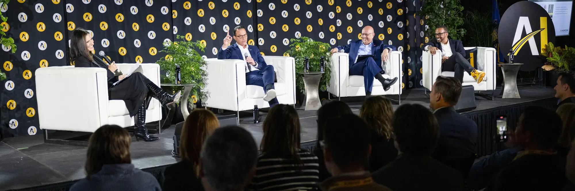 Panelists on stage in front of a black and yellow colored wall at AI Horizons.