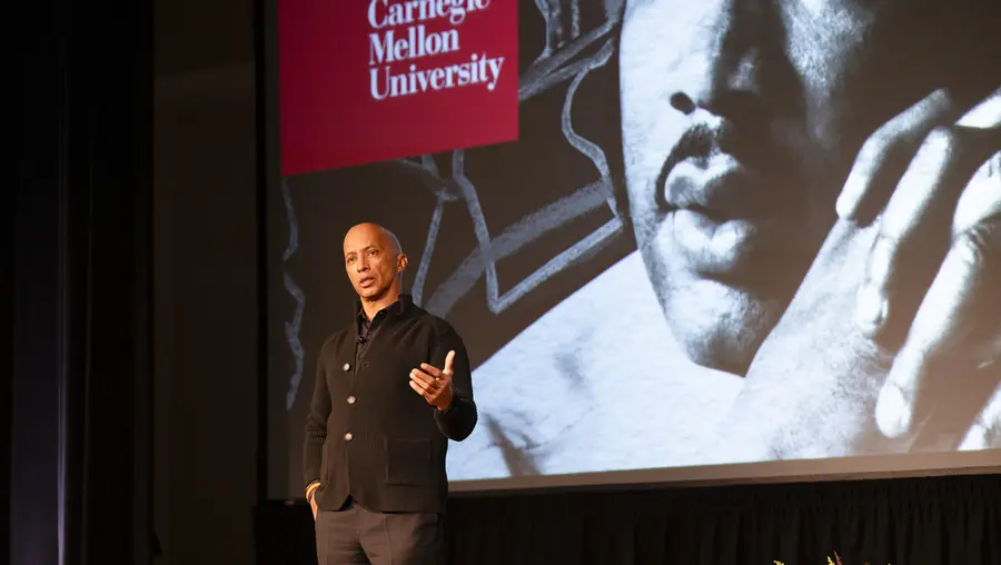 Byron Pitts on stage in front of big screen displaying image of MLK and CMU logo