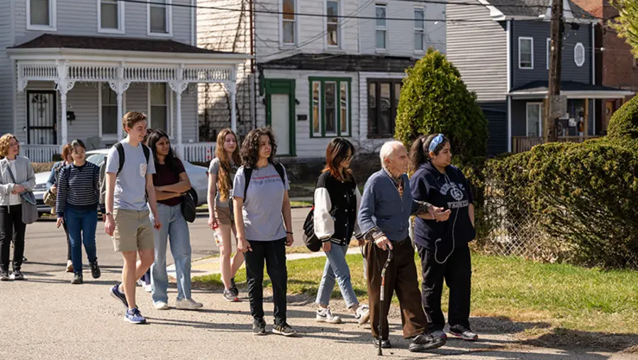 Elderly gentleman with cane leads group of students through neighborhood