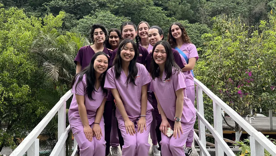 Small group of students wearing scrubs posing outdoors with trees in background