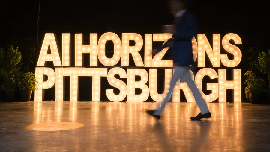 Someone walks by a large sign of the letters "AI Horizons Pittsburgh" spelled out by lightbulbs.