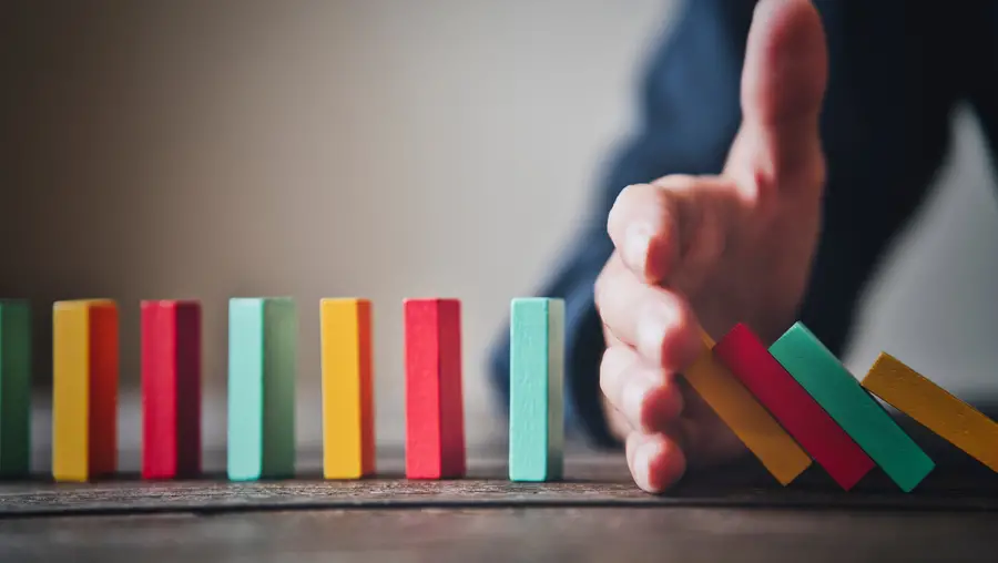 colorful dominos in a line with a hand in the middle to stop some from falling