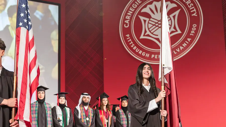 Students hold flags on stage at the CMU-Q graduation ceremony.