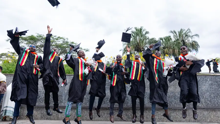CMU-Africa students in caps and gowns jump and cheer.