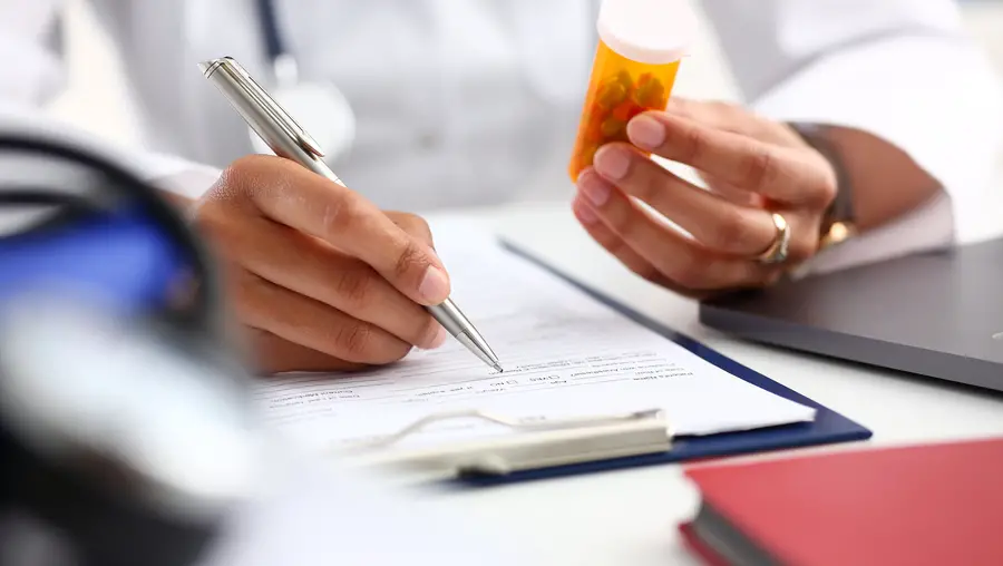 Physician holding a pill bottle, writing a note