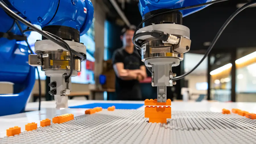 Two blue robotic arms build an orange lego guitar
