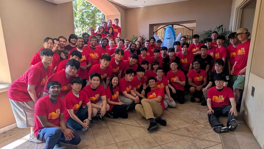 A large group of about 60 people, all wearing the same red shirt, pose and smile for a photo.